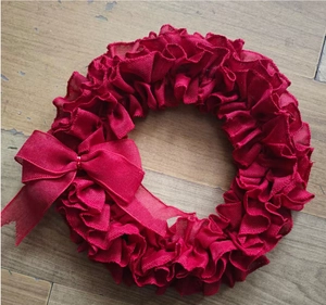 Macro shot of red burlap wreath with textured ruffles and matching bow on wooden floor