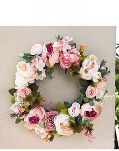 Detailed view of pink and beige faux peony wreath with green leaves on a wall