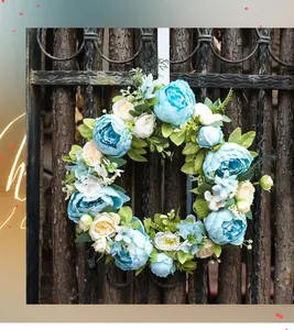 Detail of blue faux peony wreath with lush leaves on a rustic dark wooden garden gate