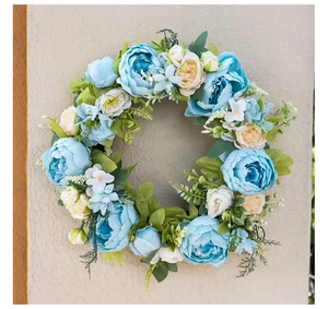 Detailed view of artificial blue peony wreath with green leaves on a textured wall
