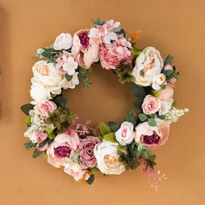 Pink peony artificial floral wreath with white roses and green leaves on wall background