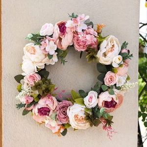 Pink and white peony artificial flower wreath with green leaves on a textured wall