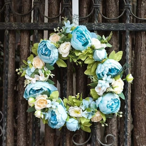 Blue and cream artificial peony floral wreath hanging on rustic wooden garden fence