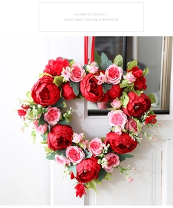 Close-up of heart-shaped peony wreath with pink and red roses hanging on a white door