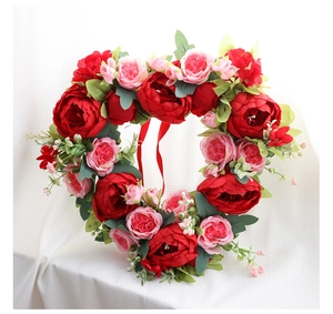 Close-up of heart-shaped floral wreath with red silk peonies and hanging ribbons