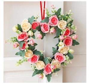 Detail of a heart-shaped floral wreath with pink roses and red ribbon on a white door
