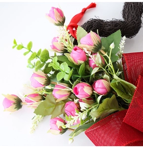 Detalle de rosas artificiales rosas con lazo de malla roja y cinta en base tejida