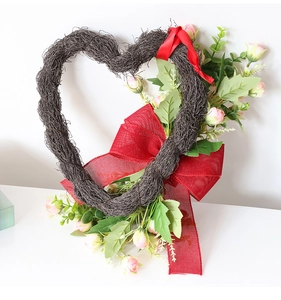 Detalle de corona de ratán en forma de corazón con rosas rosas y lazo rojo de yute