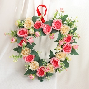 Heart-shaped floral wreath with pink roses and peonies hanging on a red ribbon string