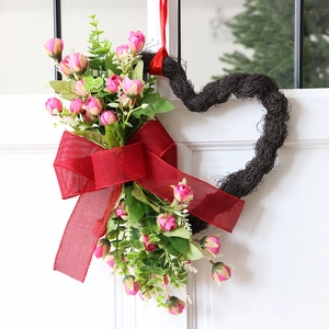 Corona en forma de corazón con rosas rosas y lazo de yute rojo en una puerta de madera