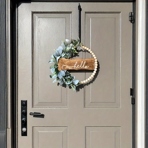 Detail of wooden bead wreath with green succulents and a hello sign on a grey door