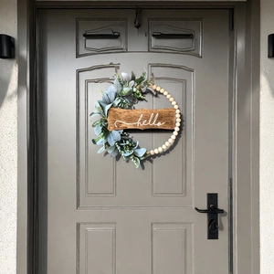 Detail of wooden bead wreath with faux greenery and a 'hello' sign on a dark door