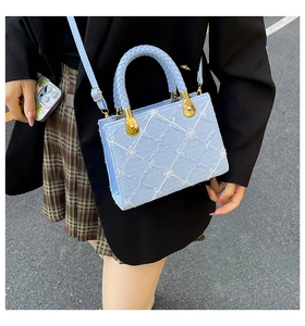Detail of woven faux leather handle on light blue quilted bag with floral pattern