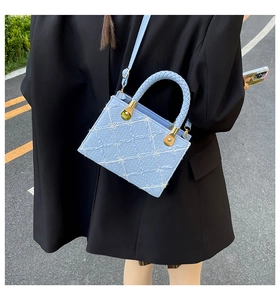Detail of light blue crossbody bag with white bow embroidery and gold hardware on street