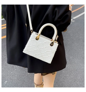Detail of a white quilted handbag with woven handle and gold drop-shaped metal clasp
