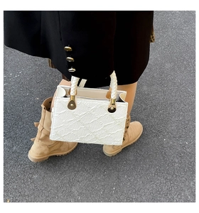 Close-up of white embossed textured handbag with gold hardware and woven handle detail