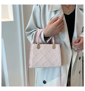 Detail of pink embossed crossbody bag featuring a woven handle and gold hardware
