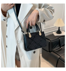 Detail of black textured crossbody bag with diamond patterns worn by model in white coat