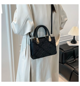Detail of black pleated tote bag showing woven handle and golden teardrop metal hardware