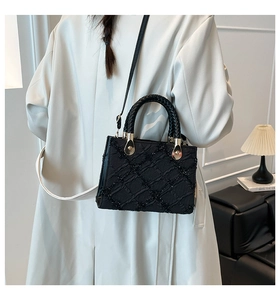 Detail of black quilted shoulder bag with sequined texture and gold hardware on model