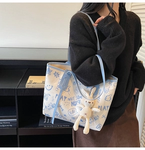 Detail of the contrast color tote bag featuring graffiti prints and a plush rabbit charm
