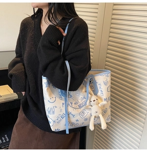 Détail du cabas en toile avec garniture en cuir bleu, motifs graffiti et breloque lapin