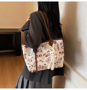 Detail of canvas tote bag featuring vintage graffiti prints and a plush bunny charm
