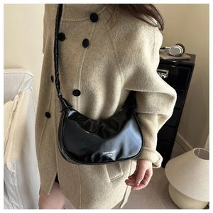 Sac baguette noir brillant avec lettrage blanc porté à l'épaule sur un manteau beige