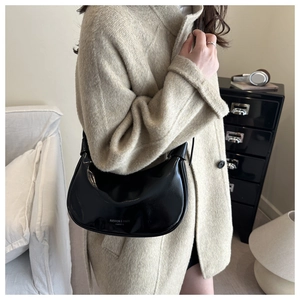 Detail of glossy black oil wax leather half-moon bag worn with a tweed coat