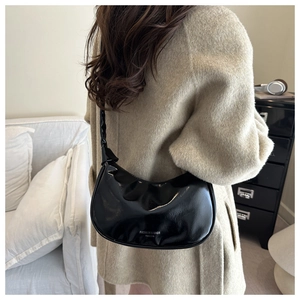 Sac bandoulière demi-lune noir brillant avec lettrage porté par un mannequin chic