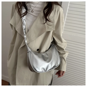Close-up of metallic silver crescent crossbody bag with wide strap on beige trench coat