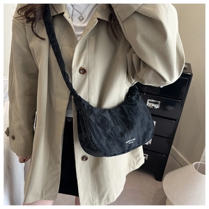 Detail of black pleated crescent crossbody bag with white branding text on durable fabric