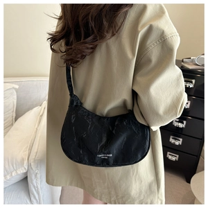 Detail showing pleated black croissant bag texture with white fashion logo on khaki coat