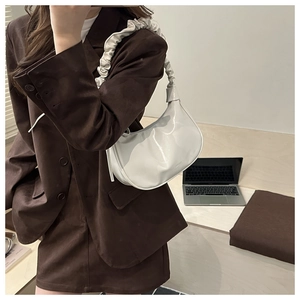 White glossy patent leather cloud bag with pleated strap shown in a professional setting
