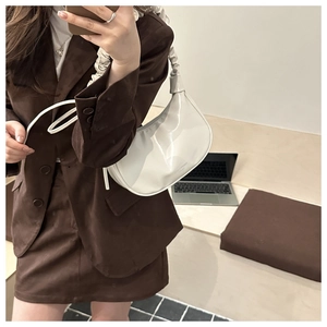 Détail d'un sac hobo en cuir verni blanc avec poignée plissée et typographie mode