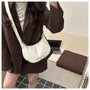 Sac demi-lune crème chic avec large bandoulière porté sur un blazer marron élégant