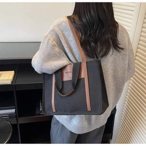 Detail of a black canvas tote bag with brown leather handles worn by a model in a library