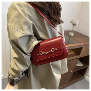 Detail of red leather shoulder bag with gold horsebit buckle on model in beige trench coat
