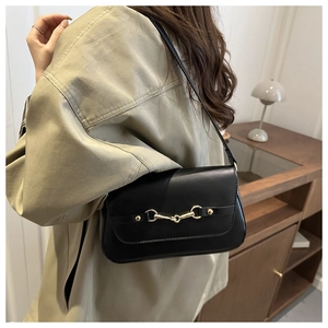 Detail of black underarm bag with gold horsebit hardware shown on model in home setting