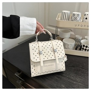 Polka dot handbag with decorative straps and silver buckles on a wooden background