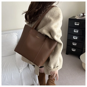 Detail of dark brown leather tote bag featuring gold embossed text on a beige coat model