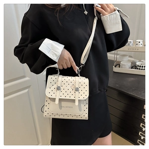 Detail of white leather crossbody bag with black polka dots and silver buckle accents