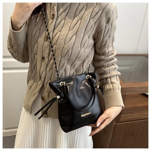 Detalle de bolso cubo negro con texto FASHION dorado, cadena y detalle de borla