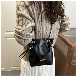 Detalle de un bolso cubo negro con cadena metálica y textura mostrado en una modelo