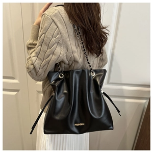 Detalle de bolso tipo cubo negro plisado con cadena dorada mostrado por una modelo
