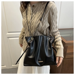 Detalle de bolso cubo negro plisado con texto fashion y correa de cadena metálica