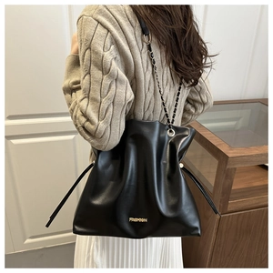 Detalle de bolso saco negro con cordón, logo dorado Fashion y correa de cadena