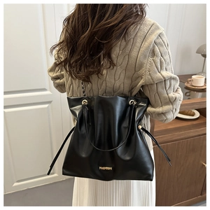 Detalle de bolso tote de cuero negro plisado con cadena de metal llevado por modelo