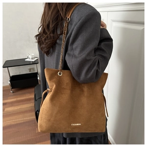 Detalle de bolso saco de ante marrón con correa de cadena y letras doradas de moda