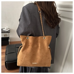 Brown suede tote bag with golden chain strap and tassel detail shown on model